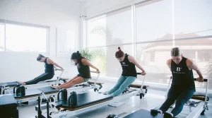 A group of women participating in a dynamic reformer Pilates class at the bright and modern Bali Pilates Plus studio in Canggu.