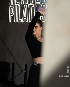 A woman working out at Revive Pilates in Canggu, with the studio's cool neon sign glowing in the background.