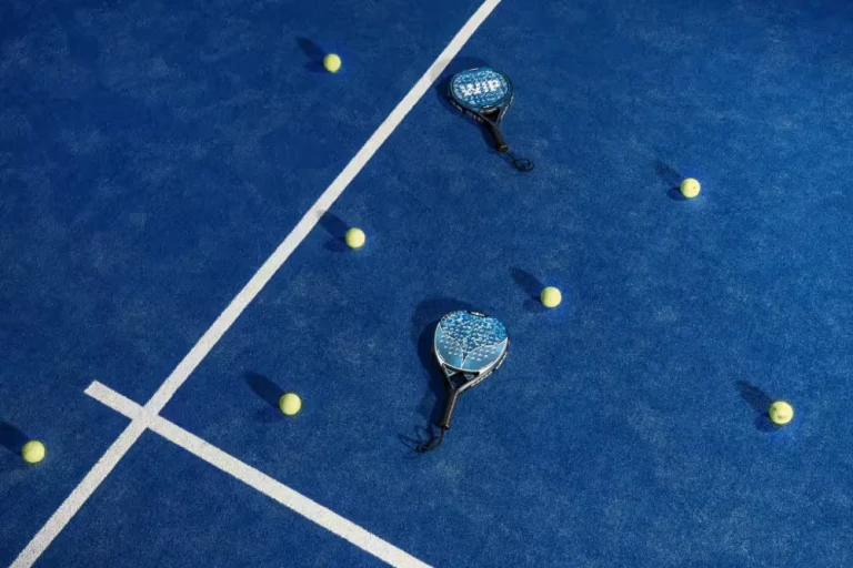 An overhead view of two padel rackets and several yellow balls scattered across a bright blue padel court in Bali.