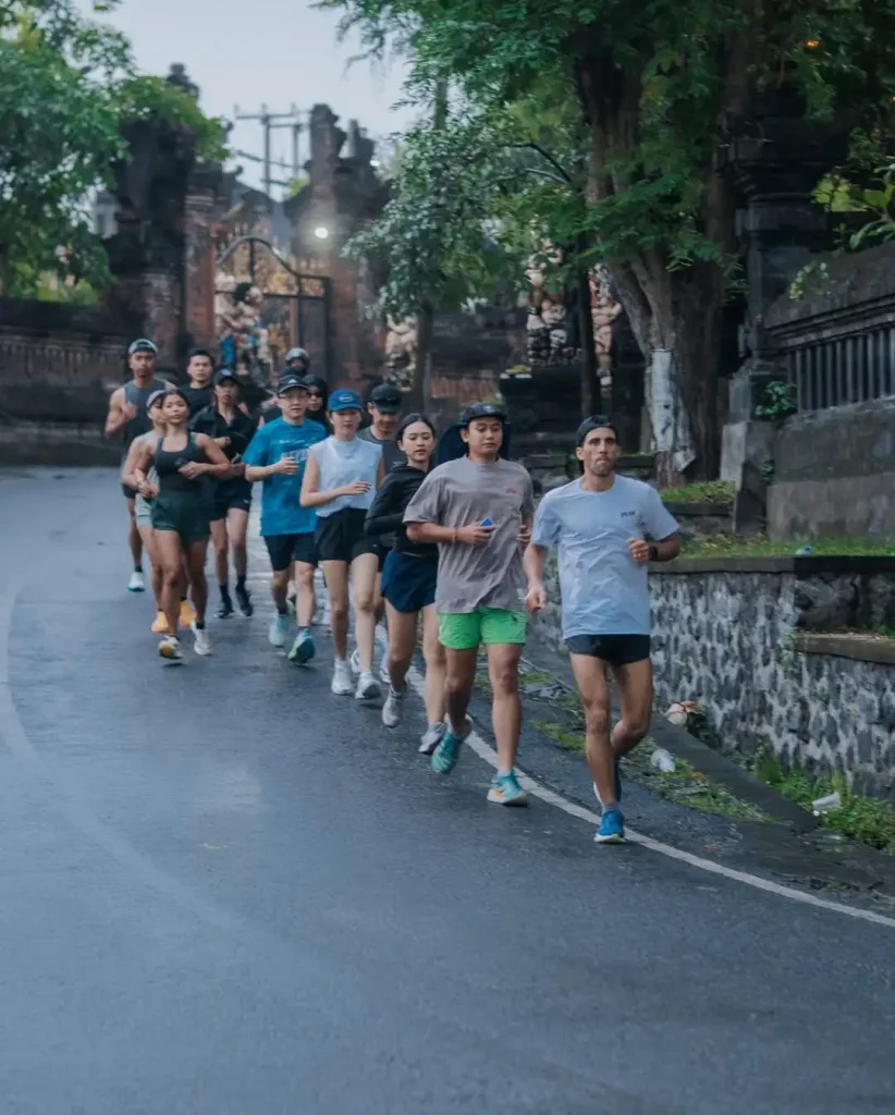 The Avenue Running Club (ARC) community running together through a scenic street in Bali, with a traditional gate in the background.