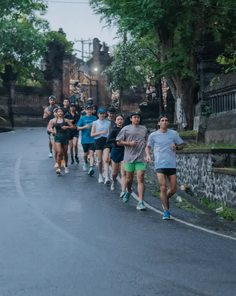 large group from the Avenue Running Club running together past a traditional Balinese gate during the 6K community run in Canggu.
