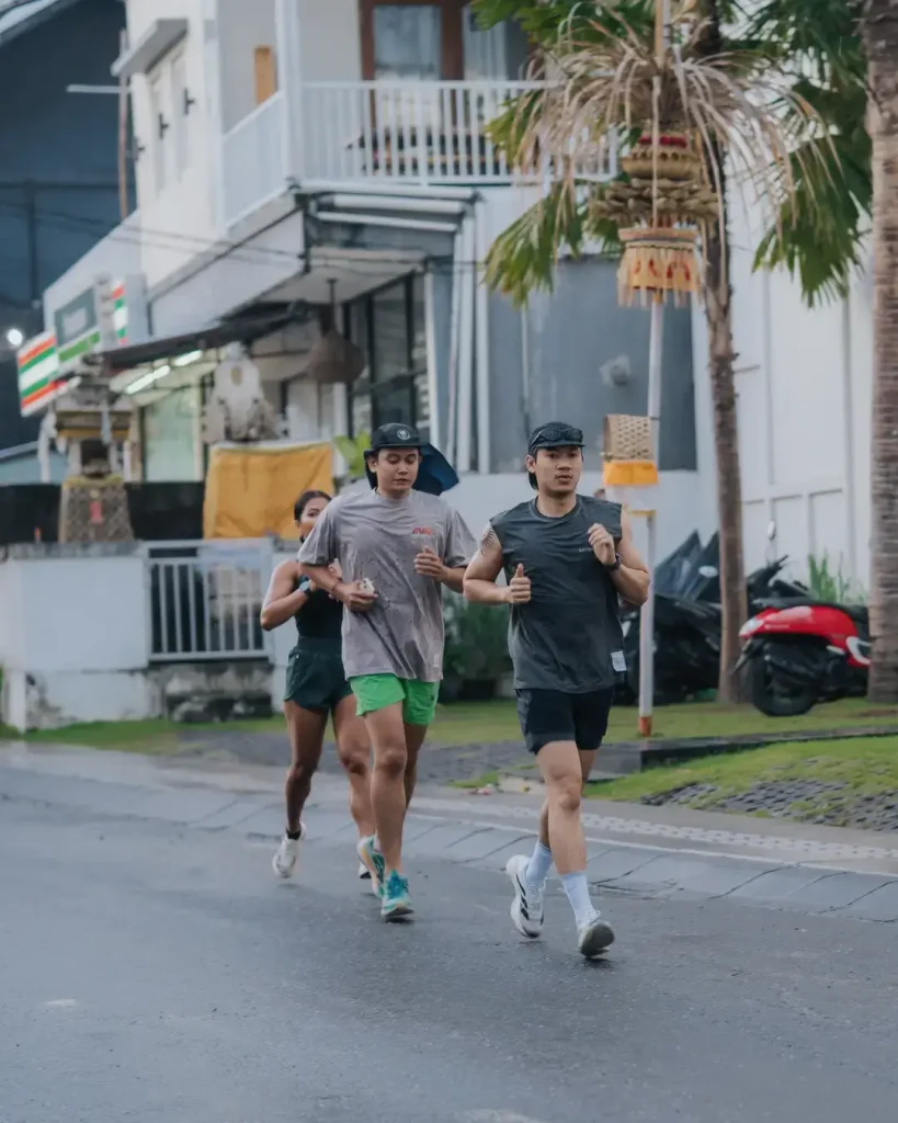 A small group of runners participating in the Avenue Running Club 6K run, with Balinese architecture and palm trees in the background.