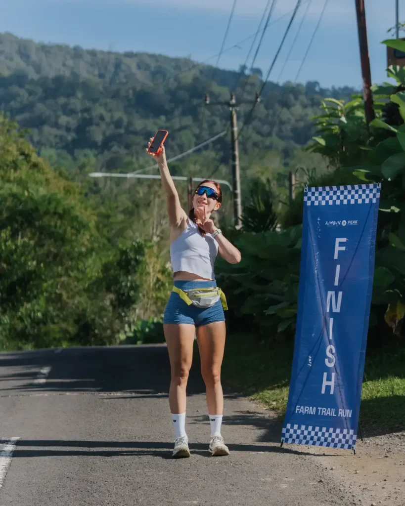 A happy participant takes a selfie next to the finish line banner after completing the Farm Trail Run at Rimbun Peak in Bali on June 15 2025.