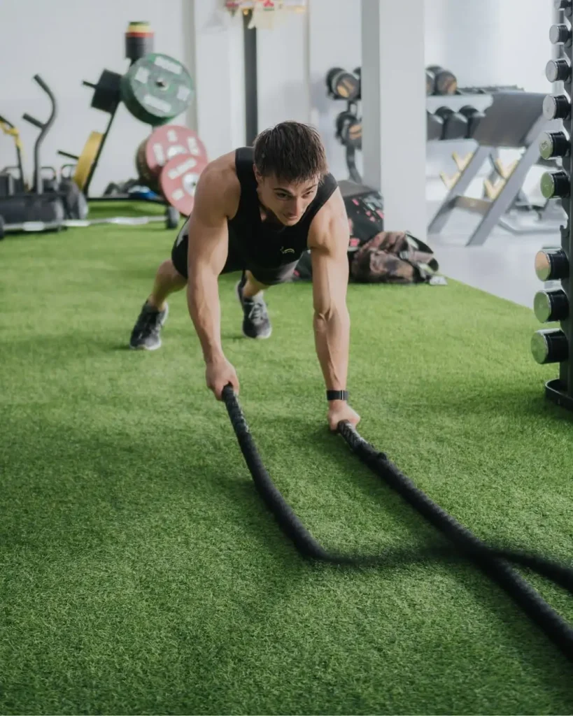 A fit man performing a dynamic battle rope exercise in a plank position on the green turf of the functional training area at Avenue Fitness.