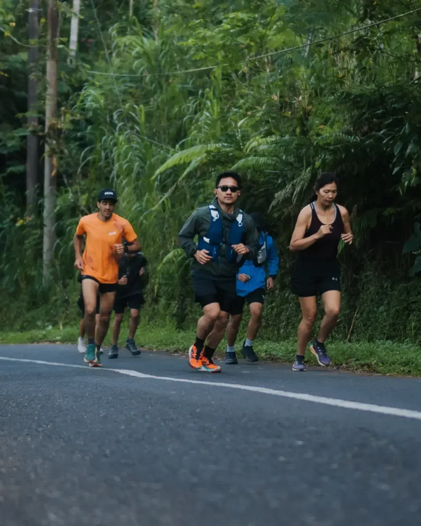 A group of participants running together on a road through a lush green landscape during the Farm Trail Run event hosted by Avenue Running Club.