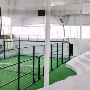 A modern, clean indoor padel court with green turf and spectator seating at Bali Padel Academy.