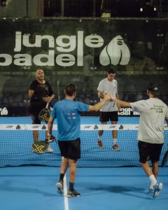 Four men shaking hands over the net after a game of padel at Jungle Padel in Canggu, with the club's logo in the background.