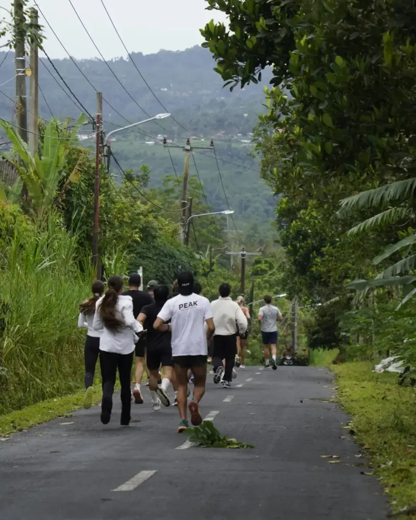 A group of participants running away from the camera on a scenic road during the Farm Trail Run event in the hills of Jempanang, Bali.