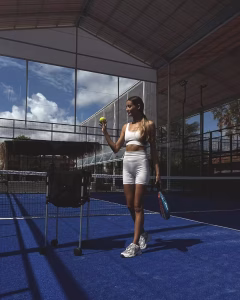 A woman in stylish athletic wear standing on a blue court, ready to serve during a game at Monkey Padel in Bali.