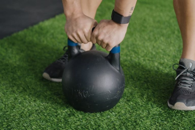 A close-up of a person's muscular arm picking up a weight from a rack, a great alternative to a kettlebell workout for building strength