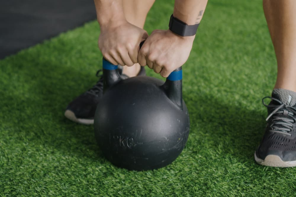 A close-up of a person's muscular arm picking up a weight from a rack, a great alternative to a kettlebell workout for building strength