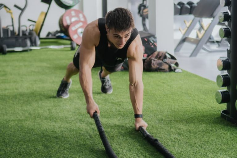 Man performing a plank with battle ropes on green turf, demonstrating a dynamic HIIT workout.