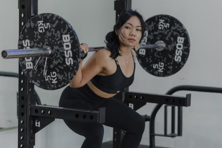 A woman performing a barbell squat as part of a full body workout in a gym.