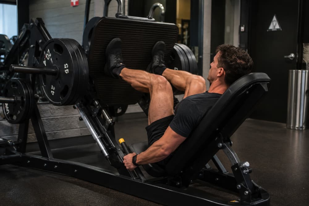 Muscular man using a leg press machine at the gym for strength training.