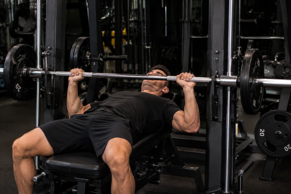 Muscular man performing an incline bench press on a Smith machine in a gym.