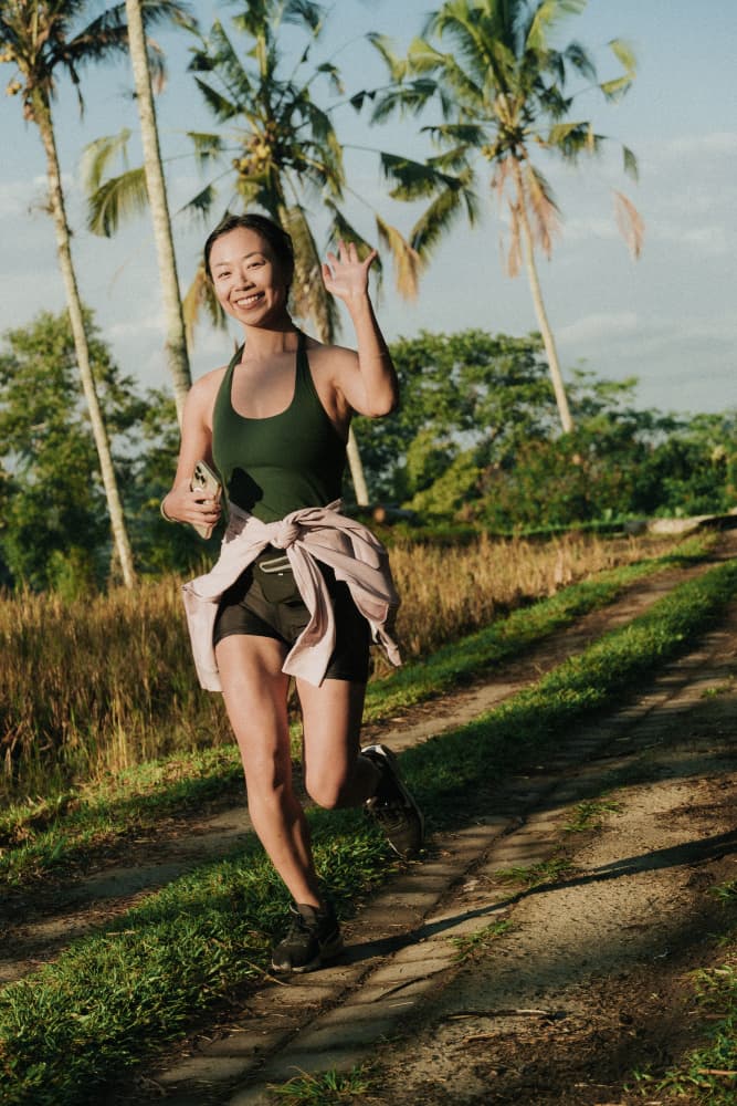 A smiling woman running on a scenic path during the Avenue Fitness Naturun event.