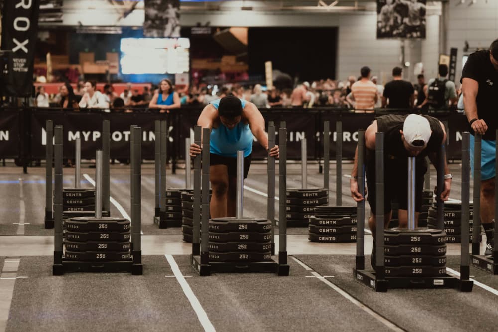 Athletes pushing heavy weight sleds during a HYROX competition indoors.