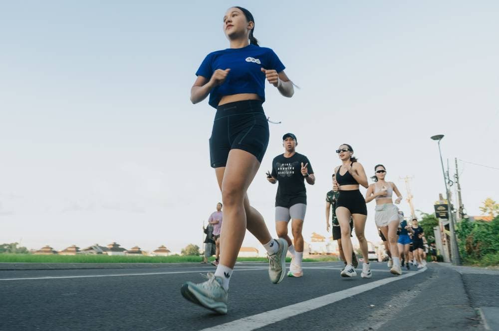 A group of runners from a local running club in Canggu jogging on a paved road during a bright day.